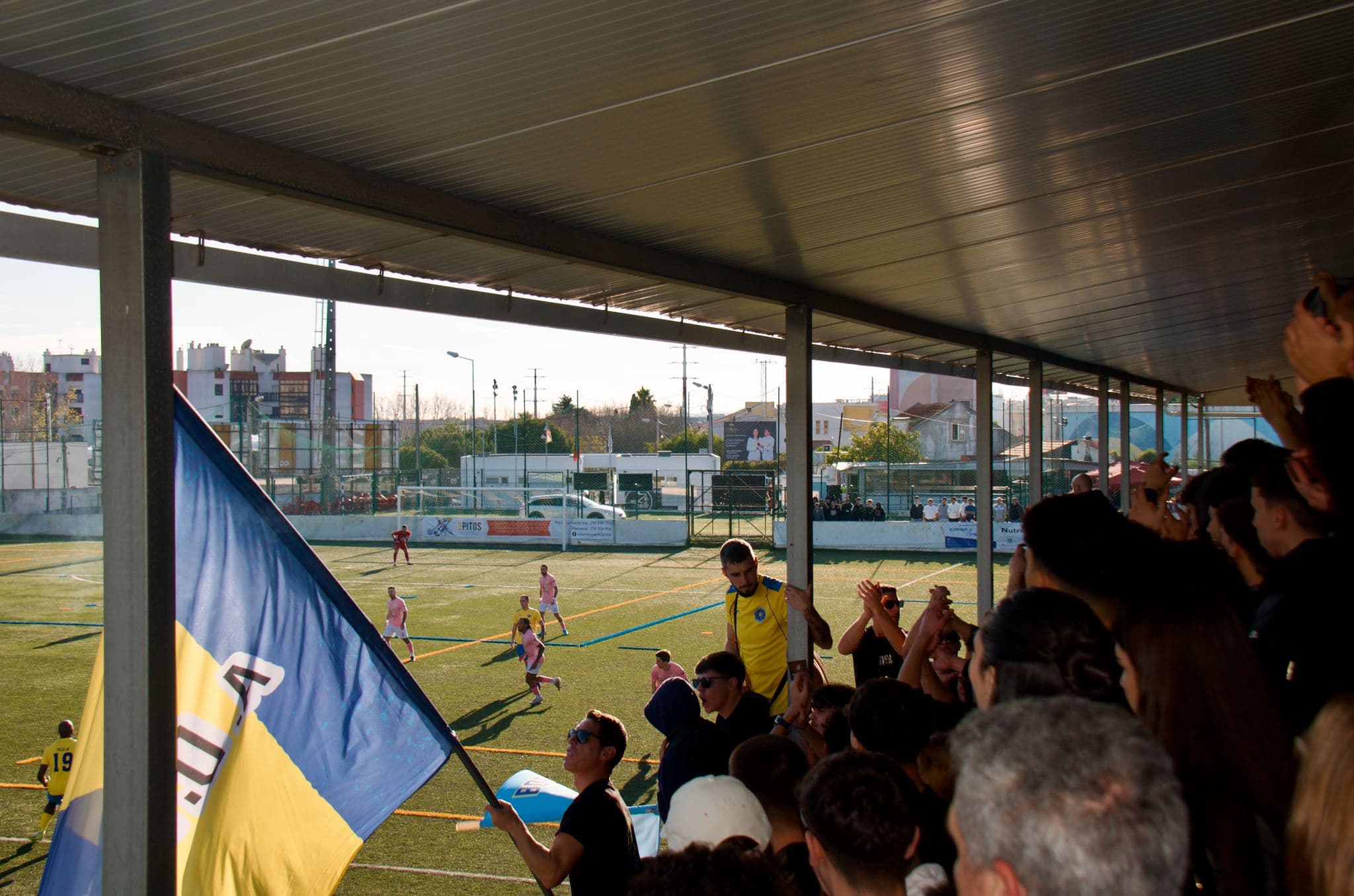 Bobadelense supporters cheering from the stand beside a large yellow and blue flag