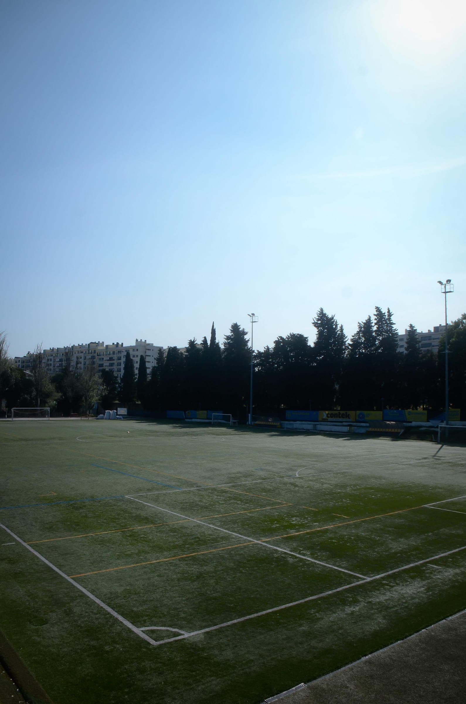 An artificial pitch ringed by trees and apartment blocks under a clear sky